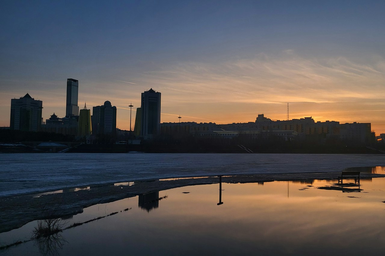 Astana's skyline silhouetted at sunset, reflected in water