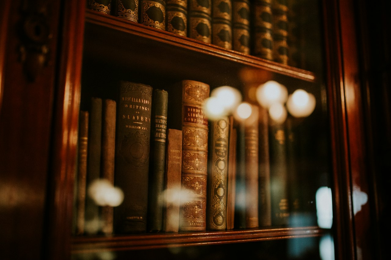 Old books behind the glass of a lit bookcase