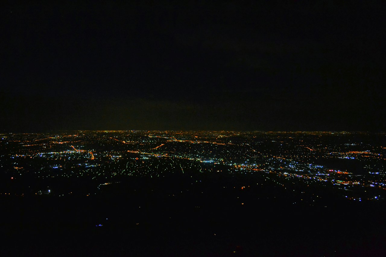 The lights of a city spread across the plain at night, seen from the hills