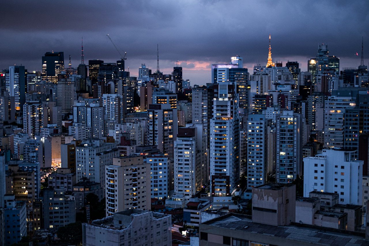 Dense São Paulo towers at blue hour, windows lit beneath a heavy grey sky