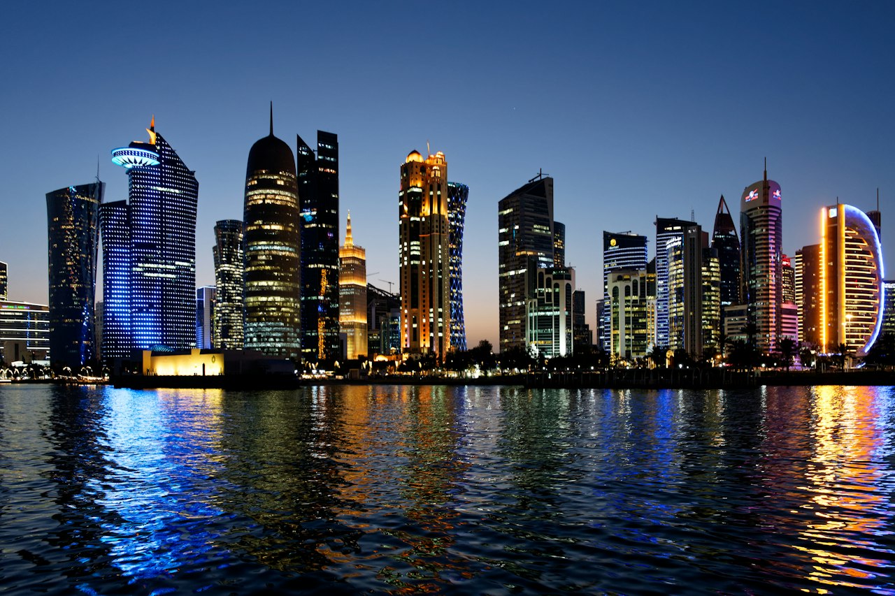 The Doha skyline across the bay at blue hour, its lights reflected in the water