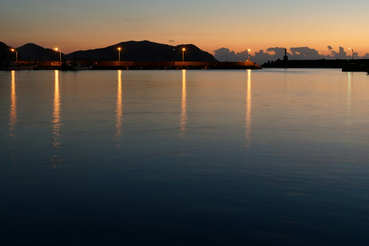 Harbour lamps reflected in still water at dusk, a lighthouse on the breakwater