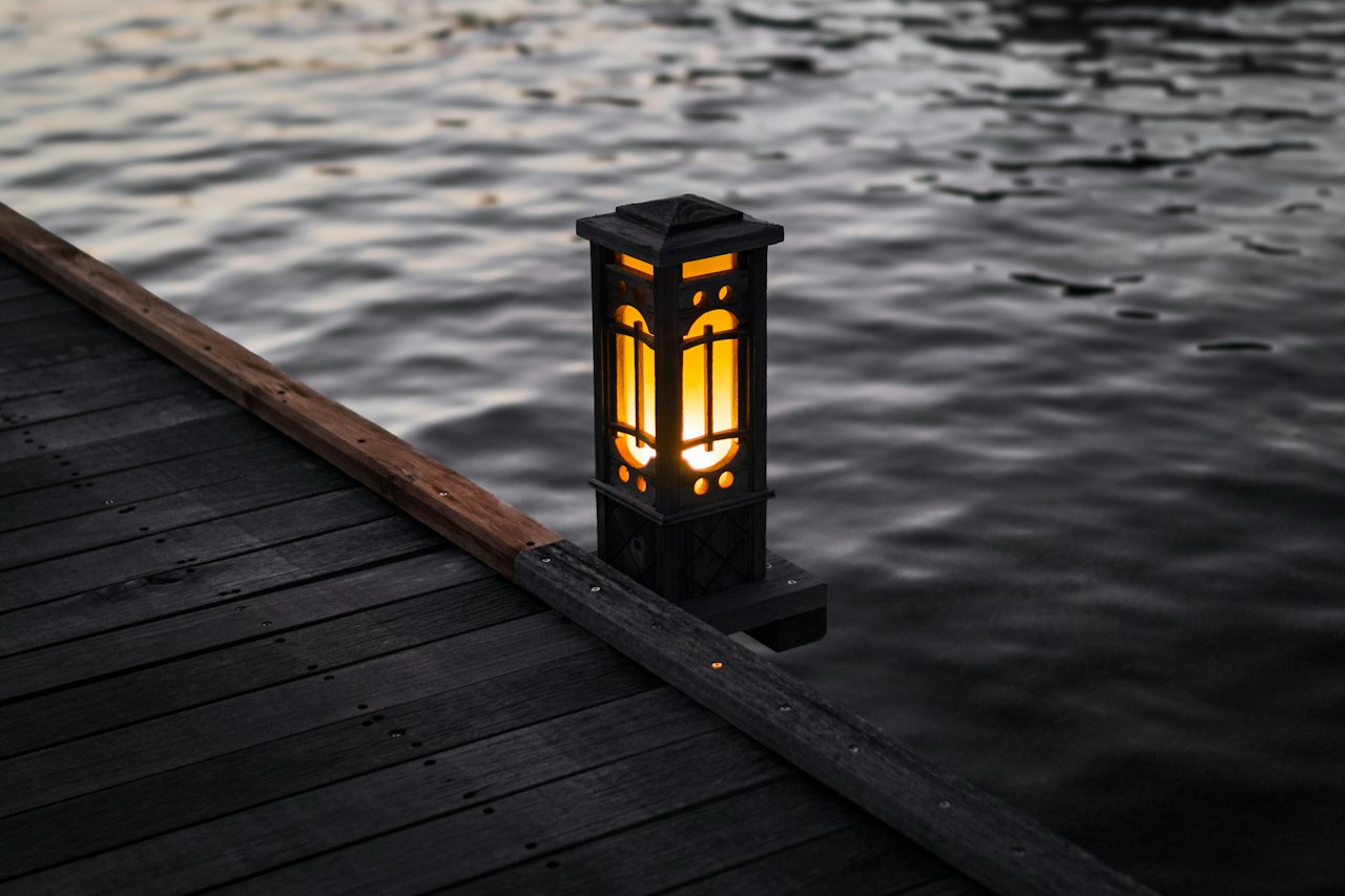 A lantern glowing on a wooden dock beside dark water
