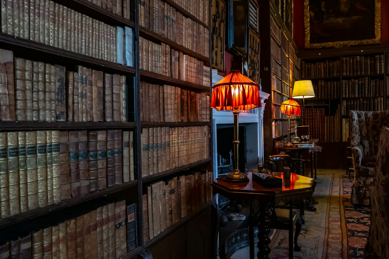 Shelves of old books in a room lit by table lamps