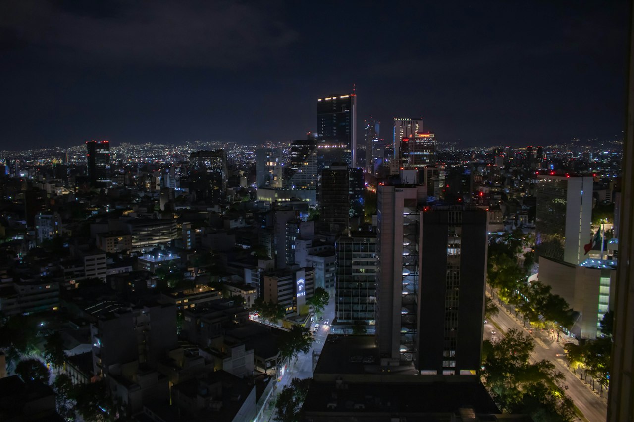 Mexico City's towers and tree-lined streets lit at night, seen from a high-rise