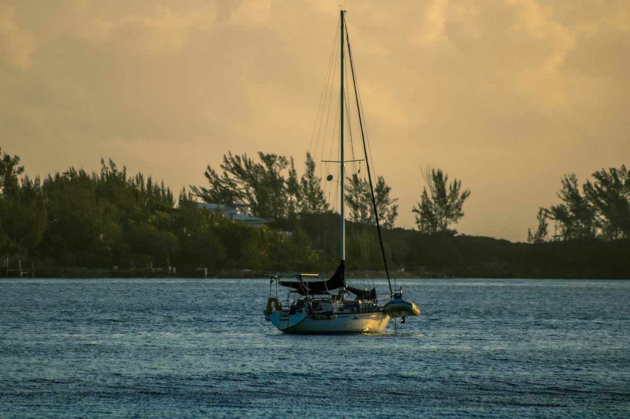 A sailboat at anchor off a tree-lined shore near Nassau in golden morning light