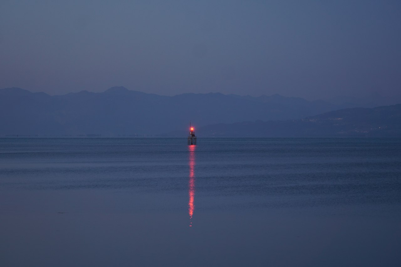 A red navigation light reflected in calm water at dusk