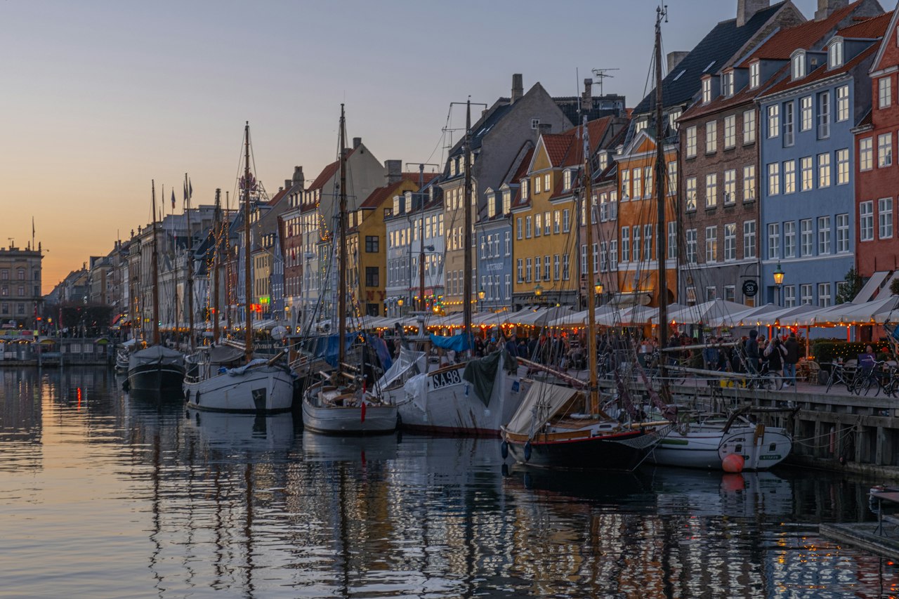 Nyhavn harbour at dusk, moored wooden boats before lit townhouses, Copenhagen