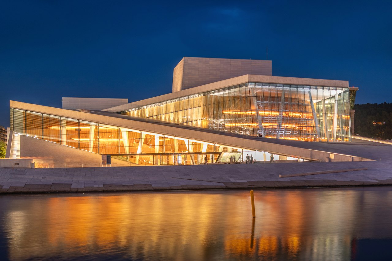 The Oslo Opera House illuminated at night, its warm lights reflected in the harbour