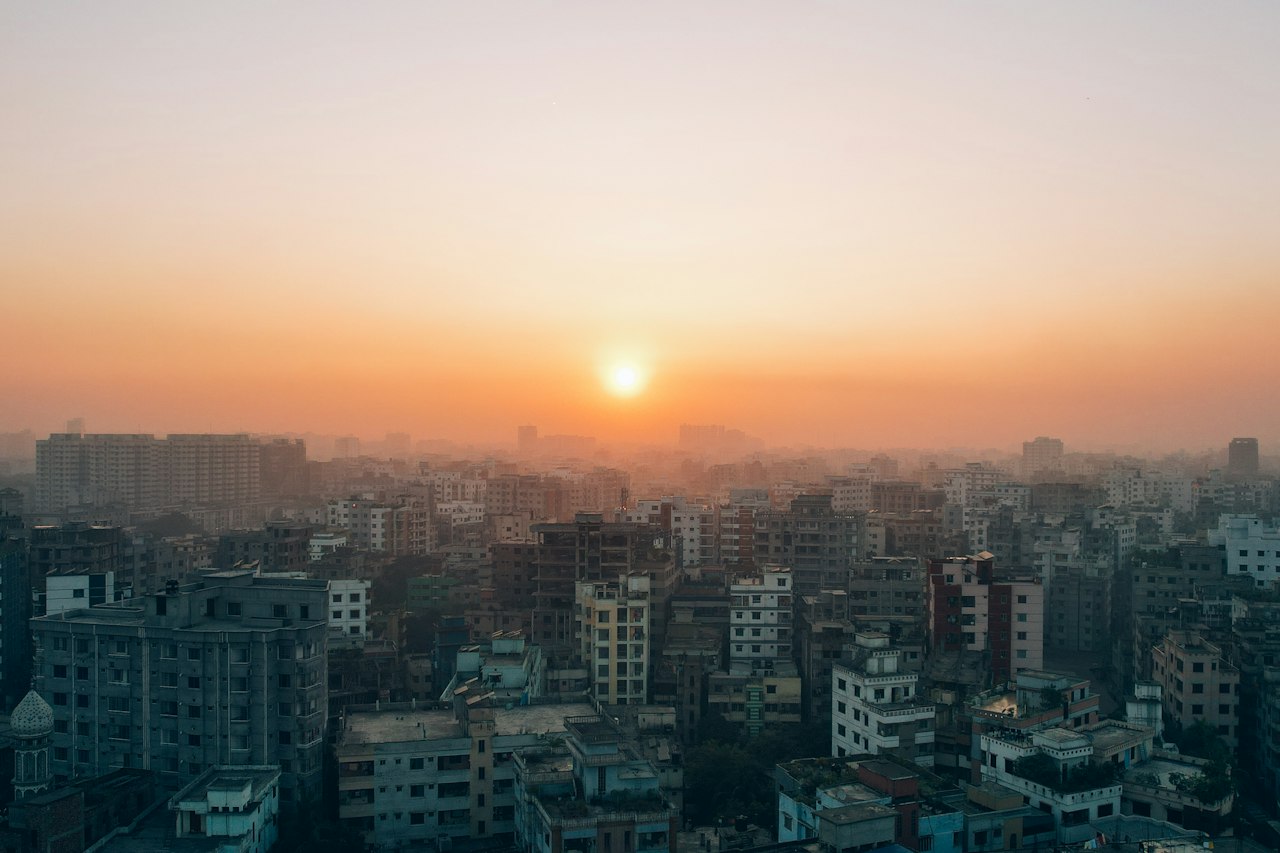 The sun setting over Dhaka's dense skyline in soft haze