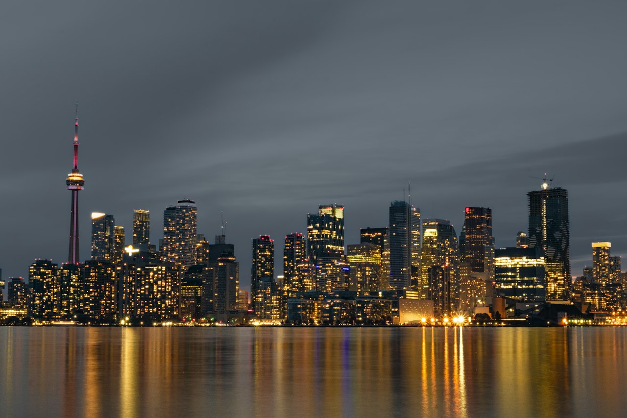 The Toronto skyline and CN Tower across Lake Ontario at dusk, city lights reflected in the water