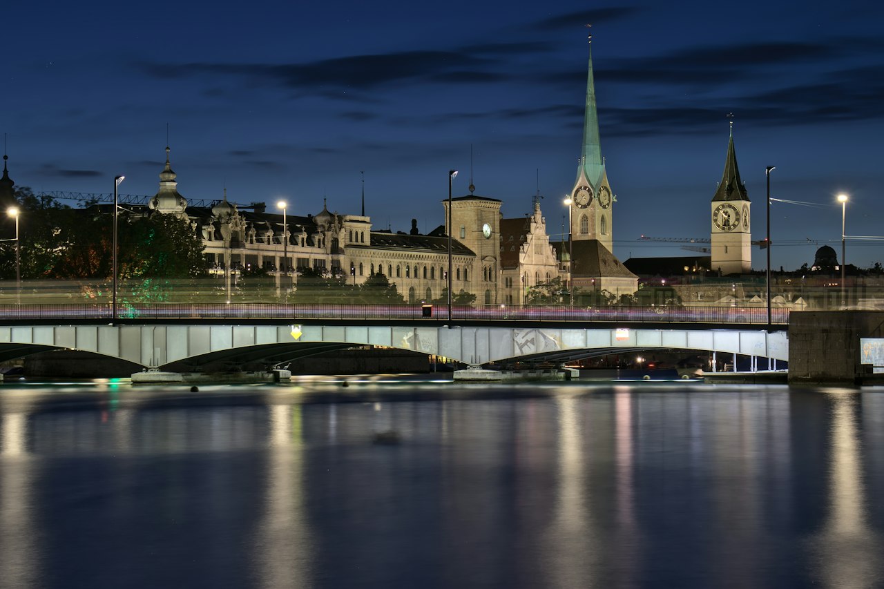 Zürich's old town spires and a lit bridge over the Limmat at dusk
